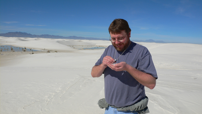 Photograph of Ken Edgett preparing to look at gypsum sand with a hand lens on a dune at White Sands National Monument in February 2007.
